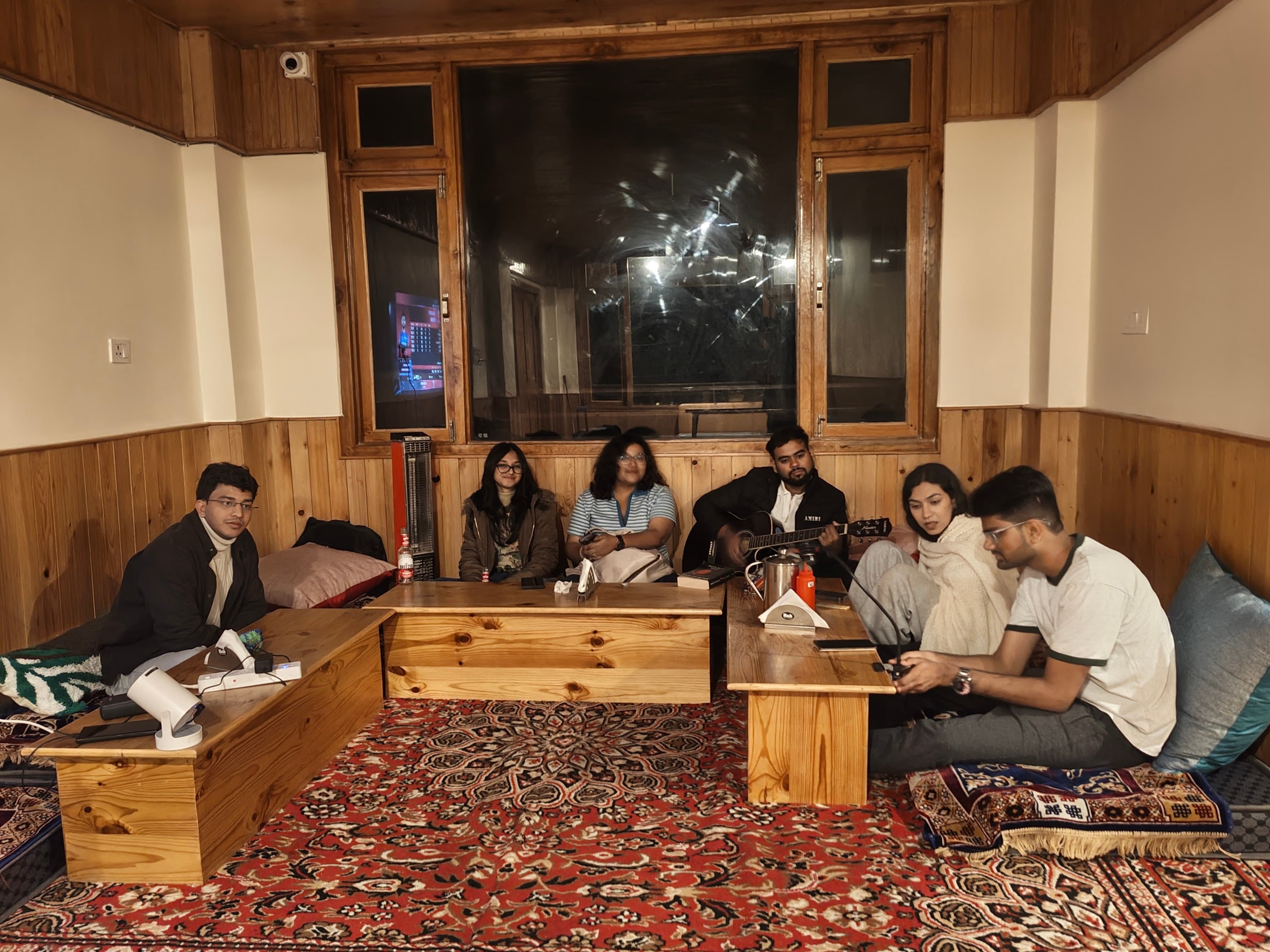 A circle of friends together at night, one with a guitar